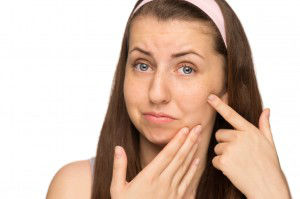Unhappy girl squeezing pimple on cheek isolated
