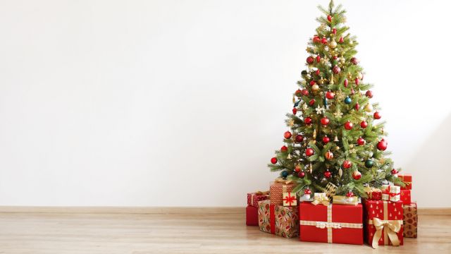 Big beautiful christmas tree decorated with beautiful shiny baubles and many different presents on wooden floor. White wall background with a lot of copy space for text. Close up.