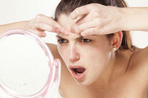 young woman squeeze her acne in front of the mirror