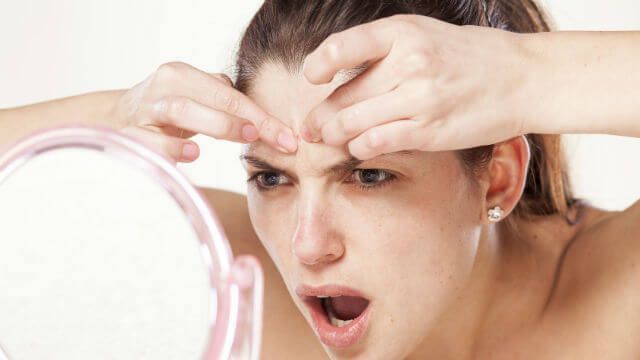 young woman squeeze her acne in front of the mirror