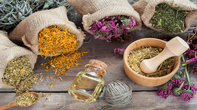 Healing herbs in hessian bags, wooden mortar with chamomile and essential oil on rustic table, herbal medicine.