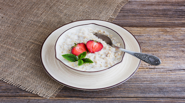 Oatmeal porridge in bowl topped with fresh strawberries on old wooden table