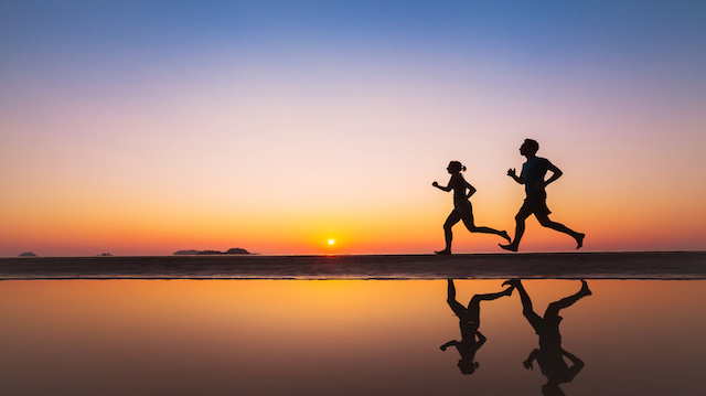 workout, silhouettes of two runners on the beach at sunset, sport and healthy lifestyle background