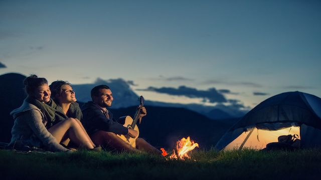 Three friends camping with fire on mountain at sunset