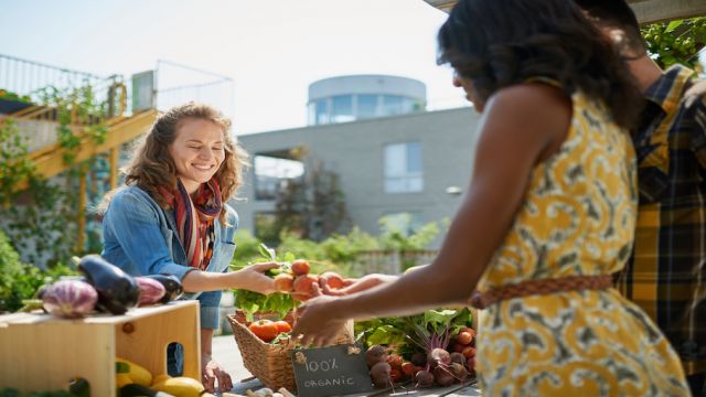 Friendly woman tending an organic vegetable stall at a farmer's market and selling fresh vegetables from the rooftop garden
