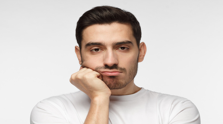 Close up portrait of bored young man in white tshirt with head on chin ...