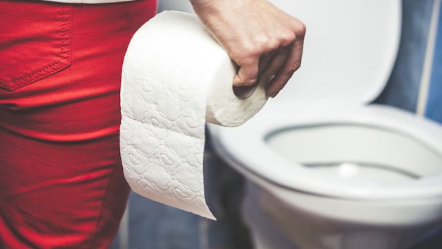 Woman suffers from diarrhea holds toilet paper roll in front of toilet bowl. Stomach upset.