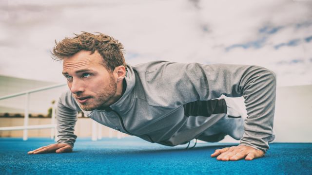Push-up exercise fitness man training arms muscles at outdoor gym. Male athlete working out with bodyweight floor exercises.