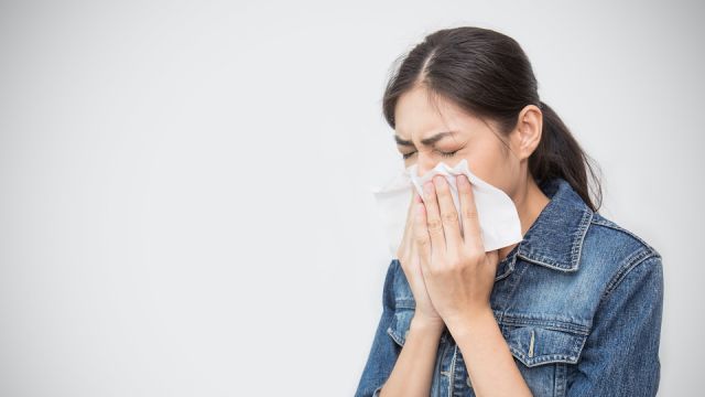 Woman with a cold blowing her runny nose with tissue. Portrait of Asian beautiful girl get sick sneezing from flu. Healthcare and medical concept.