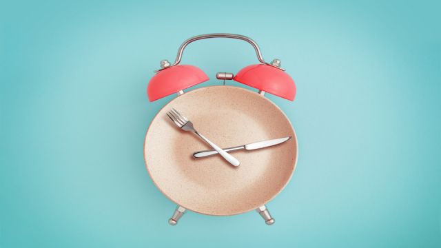 Alarm clock and plate with cutlery . Concept of intermittent fasting, lunchtime, diet and weight loss