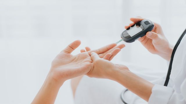 Doctor use glucosmeter checking blood sugar level from patient hand