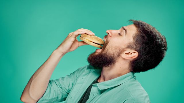 2044702 Man with a beard eating a hamburger on a green background, portrait, emotion