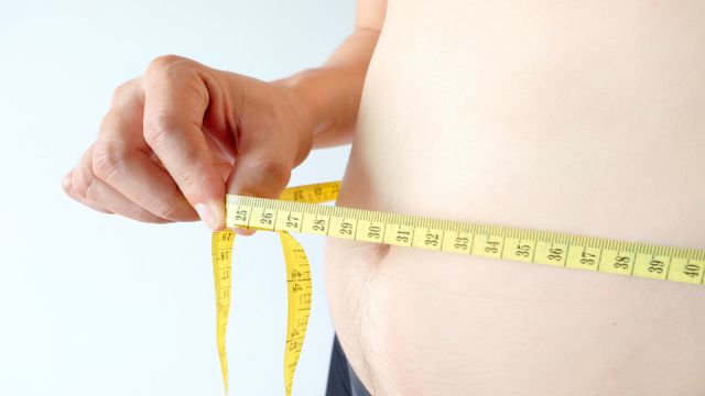 Hands of fat overweight man Measuring his waist size with a yellow measuring tape.