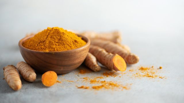 Turmeric powder in wooden bowl and fresh turmeric root on grey concrete background. Banner with copy space