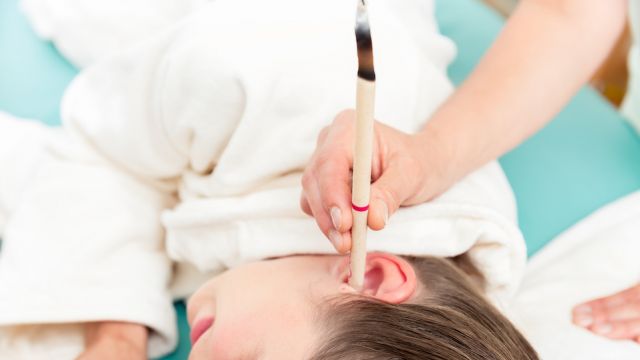 Therapist hand with burning ear candle in woman's ear