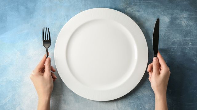 Female hands with cutlery and empty plate on color background