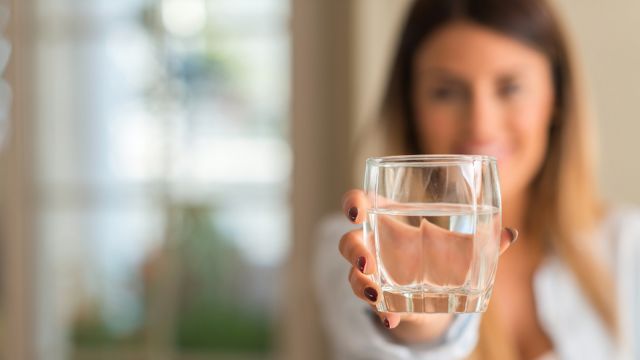 Beautiful young woman smiling while holding a glass of water at home. Lifestyle concept.