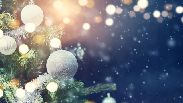 Christmas holiday background. Silver bauble hanging from a decorated on tree with bokeh and snow, copy space.