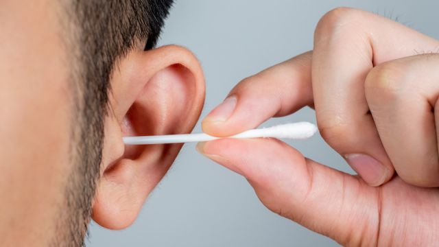 A young man asia using a stick of cotton swab for ears cleaning. Daily hygiene. Light gray background. Close up.
