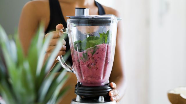 Woman blending spinach, berries, bananas and almond milk to make a healthy green smoothie