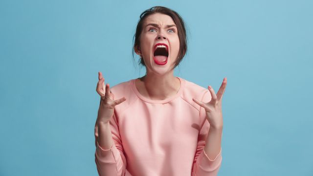 The young emotional angry woman screaming on blue studio background