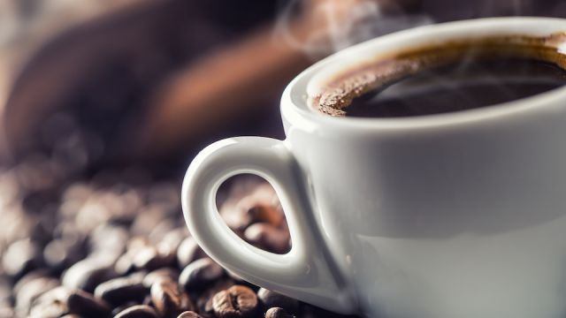 Cup of black coffee with beans on wooden table