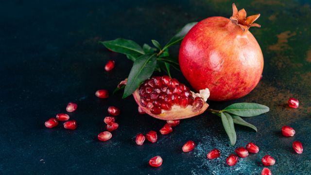 Red juice pomegranate on dark background. Ripe pomegranate with leaves on a dark background