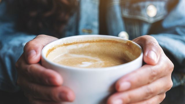 Closeup image of a woman holding a cup of hot latte coffee on the table
