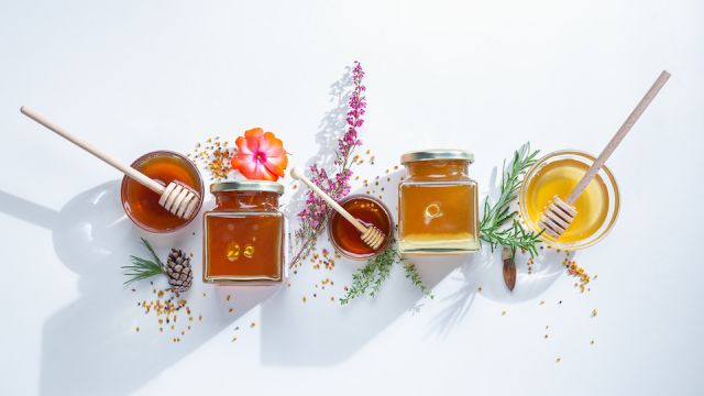 Composition of honey jars with honey sticks ,flowers and bee pollen on white background