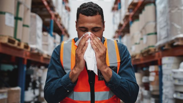 Young sick african warehouse worker blowing nose while working wearing safety vest