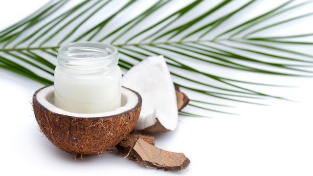 ripe coconut and organic coconut oil in glass jar with coconut leaf isolated on white