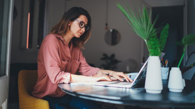 Young female entrepreneur working remotely from a home office using modern laptop computer, woman copywriter working online