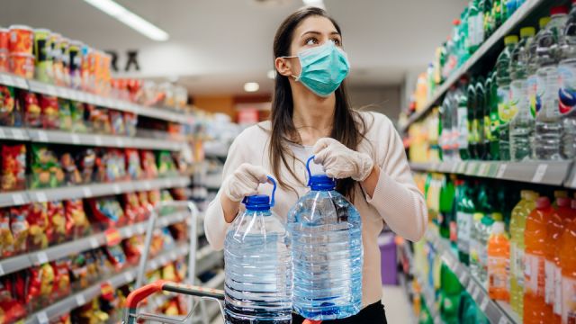 Woman wearing face mask buying bottled water in supermarket/drugstore with sold-out supplies.Prepper buying bulk supplies due to Covid-19 or Coronavirus and panic buying concept.