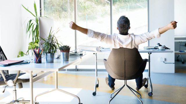 Businessman at the desk in his office stretching arms.