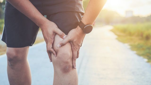 Injury from workout concept : Asian man use hands hold on his knee while running on road in the park. Shot in morning time, sunlight and warm effect with copy space for text or design
