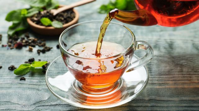 Pouring black tea into glass cup on wooden table