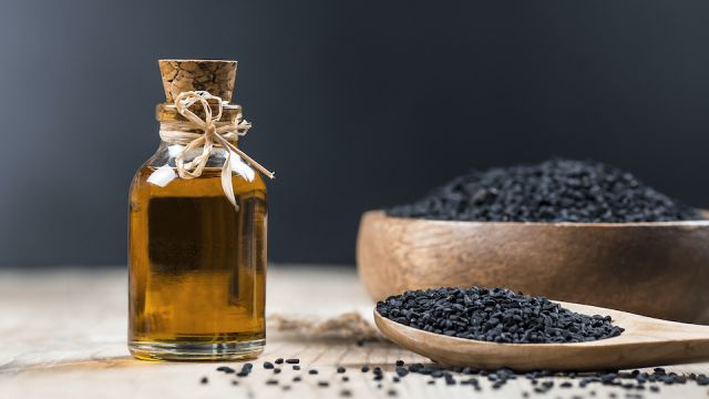 glass bottle of black cumin seeds essential oil , Nigella Sativa in spoon on wooden background. Organic herbal medicine for many diseases, black cumin