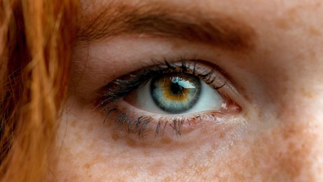 Close up macro face of young red ginger freckled woman with beautiful green eyes