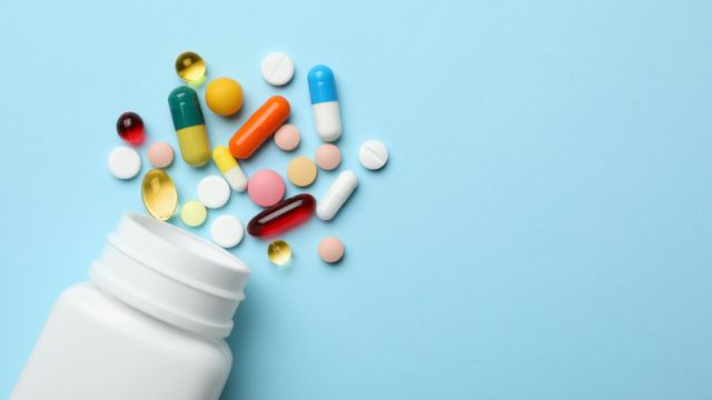 Bottle and scattered pills on color background, top view. Space for text