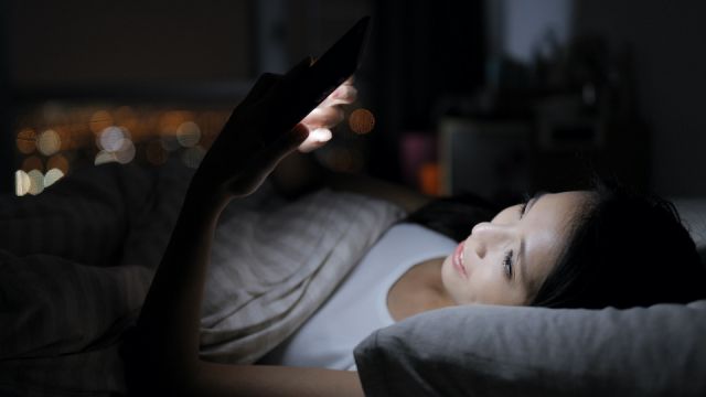 Asian Woman looking at smart phone and lying on bed