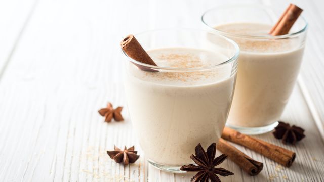 Homemade eggnog with grated nutmeg and cinnamon on white wooden table. Traditional Christmas drink.