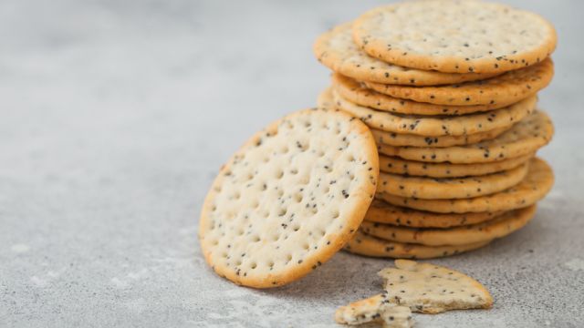 Stack of various organic crispy wheat flatbread crackers with sesame and salt on light kitchen table background.