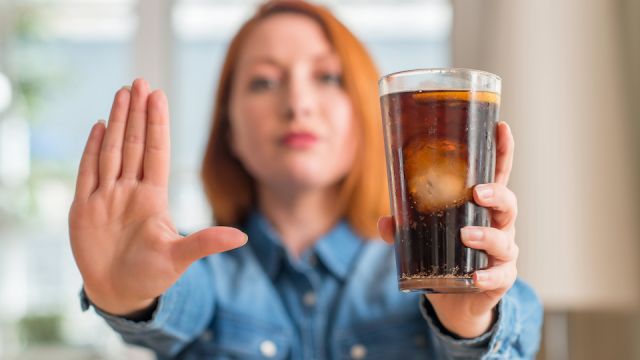 Redhead woman holding soda refreshment with open hand doing stop sign with serious and confident expression, defense gesture