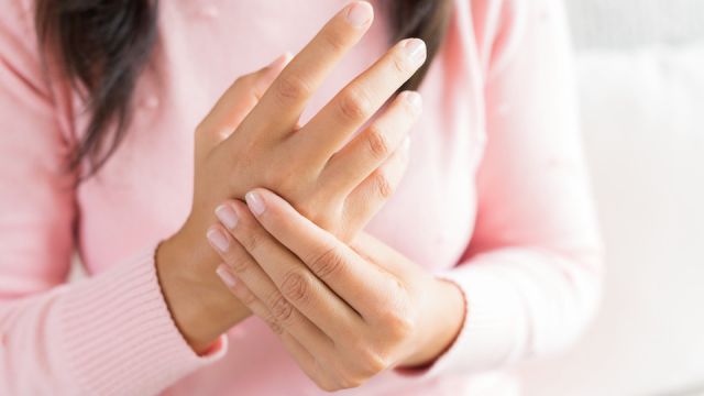 Closeup woman sitting on sofa holds her wrist hand injury, feeling pain. Health care and medical concept.